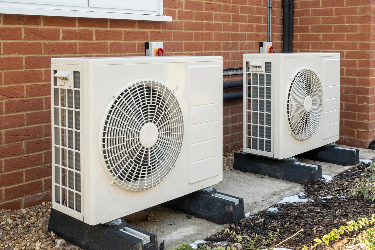 Twee witte buitenunits van een airco op rubberen voeten tegen een bakstenen gevel
