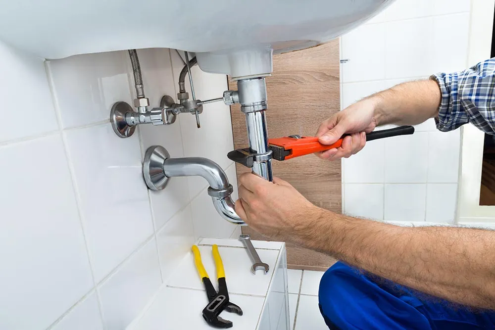 Loodgieter draait met een waterpomptang de sifon onder een wastafel vast