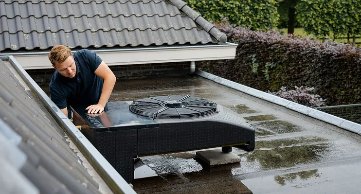 Monteur controleert een zwarte buitenunit van een warmtepomp op een plat dak